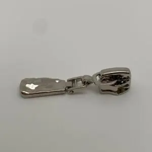Seitenansicht des Zipper Smashed Silber für 6,5 mm breite Spiralreißverschlüsse – die unregelmäßige gehämmerte Struktur des Anhängers ist besonders gut zu erkennen.