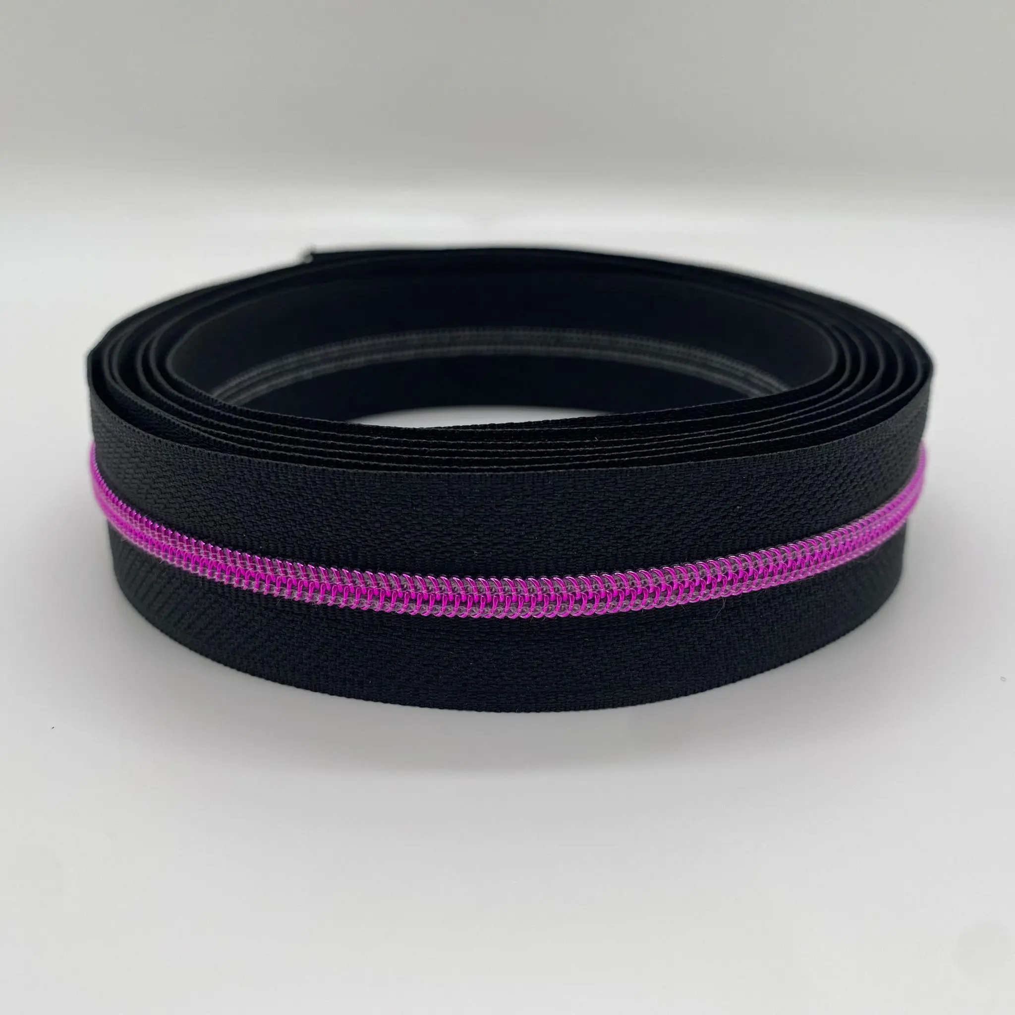 Aufgerollter Reißverschluss Intense Colors Pink schwarz mit schwarzem Band und metallisierter pinker 4,2-mm-Spiralraupe als Meterware für Taschen und DIY-Projekte.