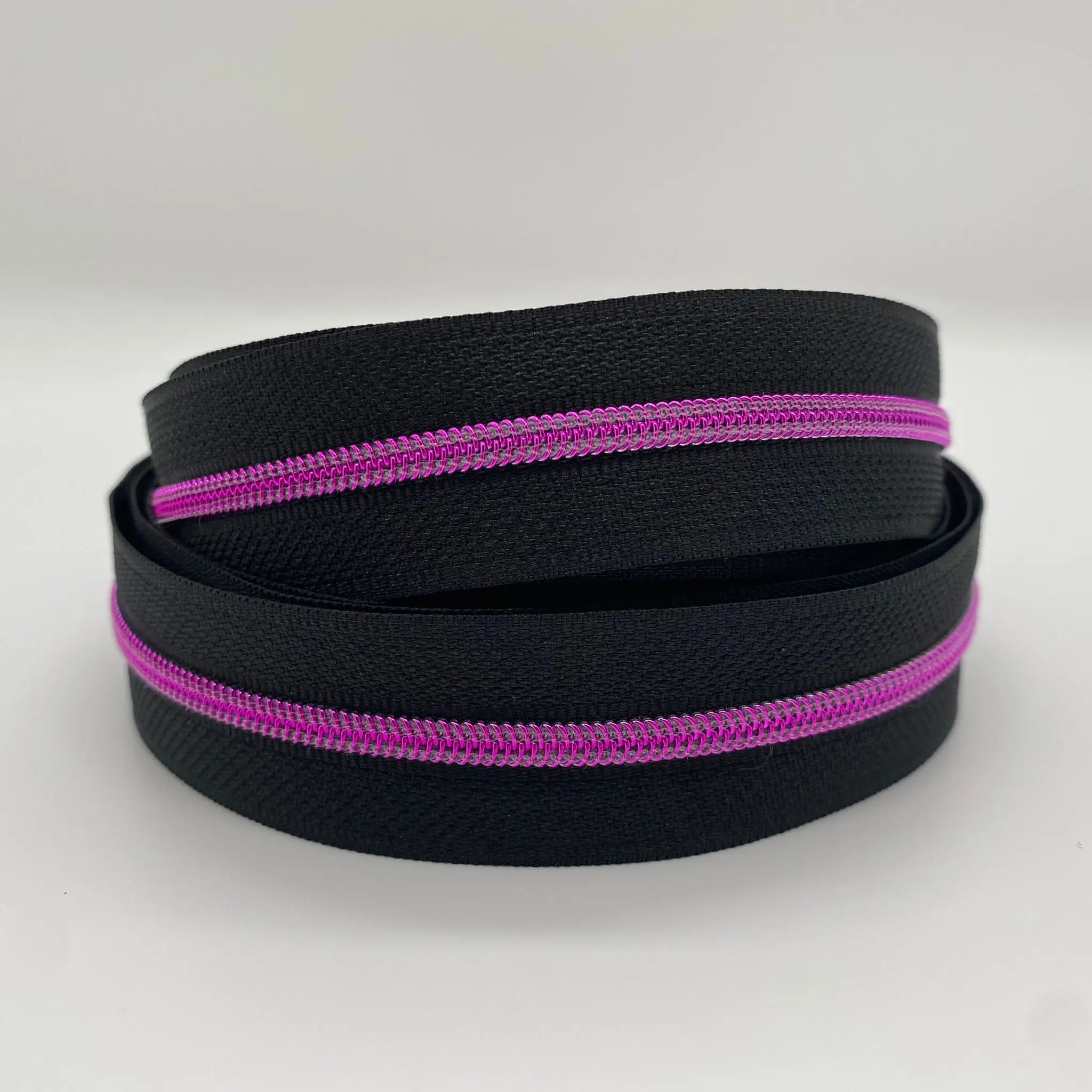 Doppelt aufgerollter Reißverschluss Intense Colors Pink Schwarz schmal mit schwarzem Band und leuchtend pinkfarbener metallisierter Spiralraupe für kreative Taschenprojekte.