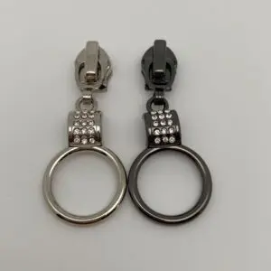 Zipper Crystal Loop für 6,5 mm breite Spiralreißverschlüsse in den beiden erhältlichen Farben Silber und Gunmetal mit Ring-Anhänger, Kristallsteinen und Autolock-Funktion.