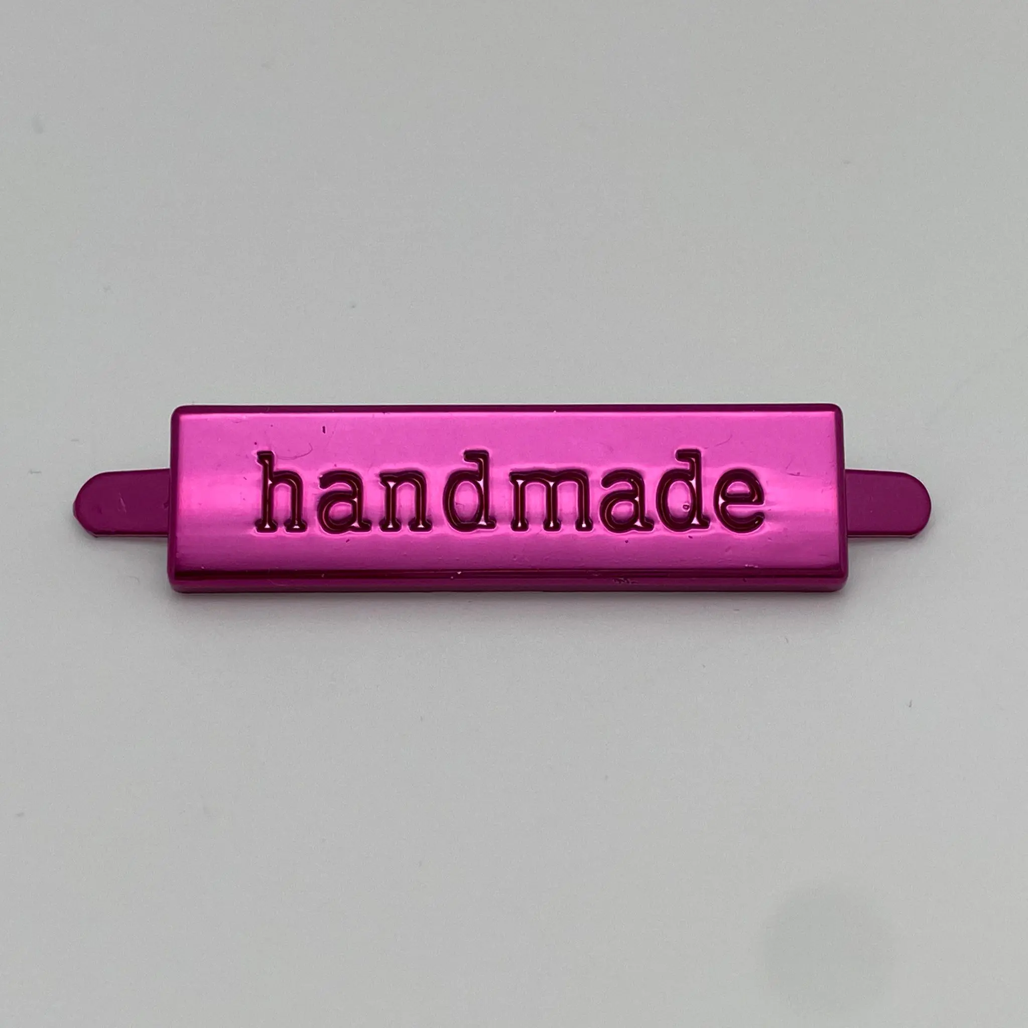 Metalllabel Handmade Pink in der Vorderansicht mit eingeprägtem Schriftzug und glänzender Metalloberfläche